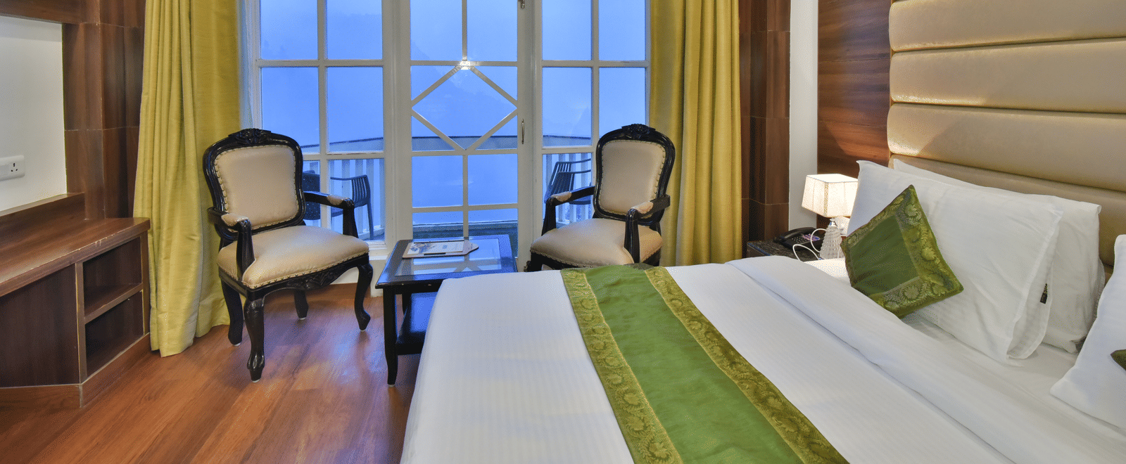 A large bed next to two chairs placed near a large window in the Premium Room at DLS Highland Resort and Spa, Mussoorie.