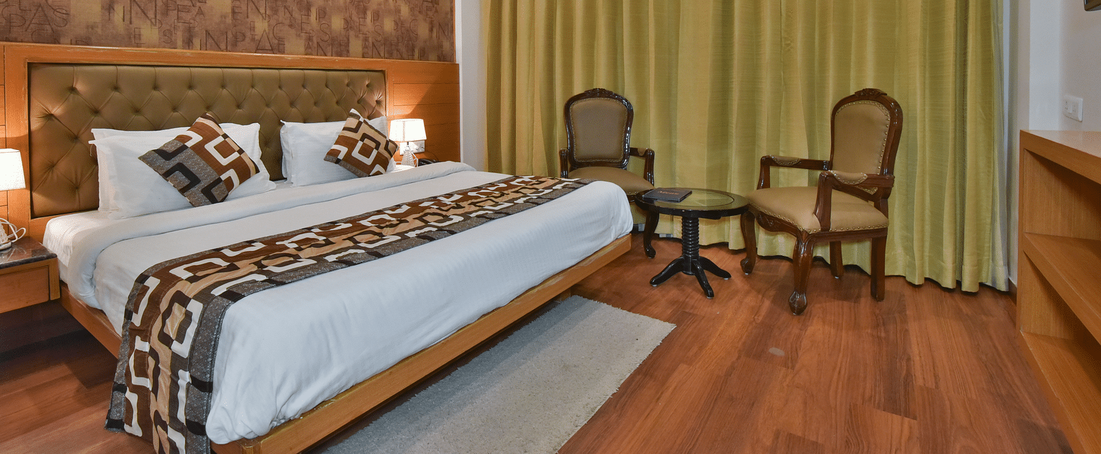 A large bed placed next to two chairs in the Deluxe Room at DLS Highland Resort and Spa, Mussoorie.