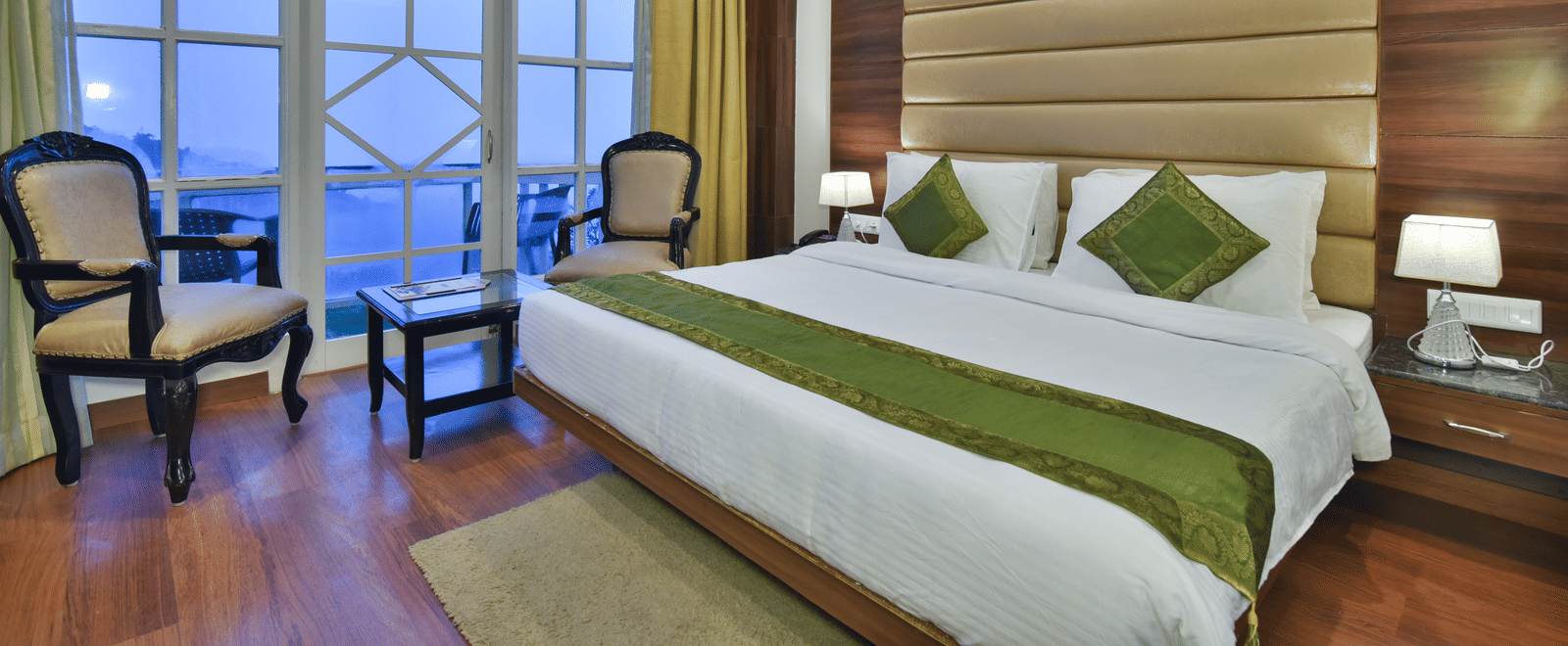 A large bed next to two chairs placed near a large window in the Premium Room at DLS Highland Resort and Spa, Mussoorie.