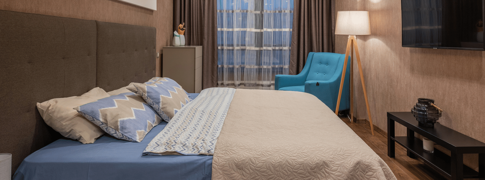 Cosy hotel room with large bed, soft lighting, modern decor, and a wall-mounted TV