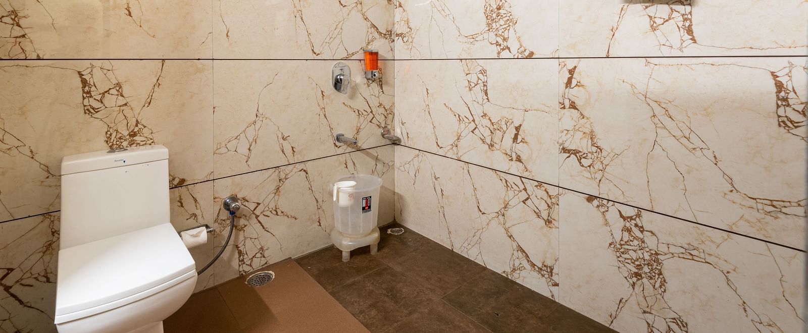 Image of a commode in a bathroom that has textured tiles on the wall and a towel holder | DLS Anupam Resort, Dharamshala