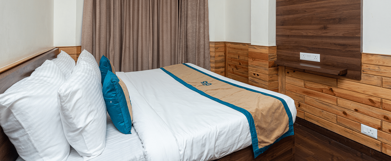 A closeup shot of the king size bed in the hotel room and a television cabinet | DLS Anupam Resort, Dharamshala