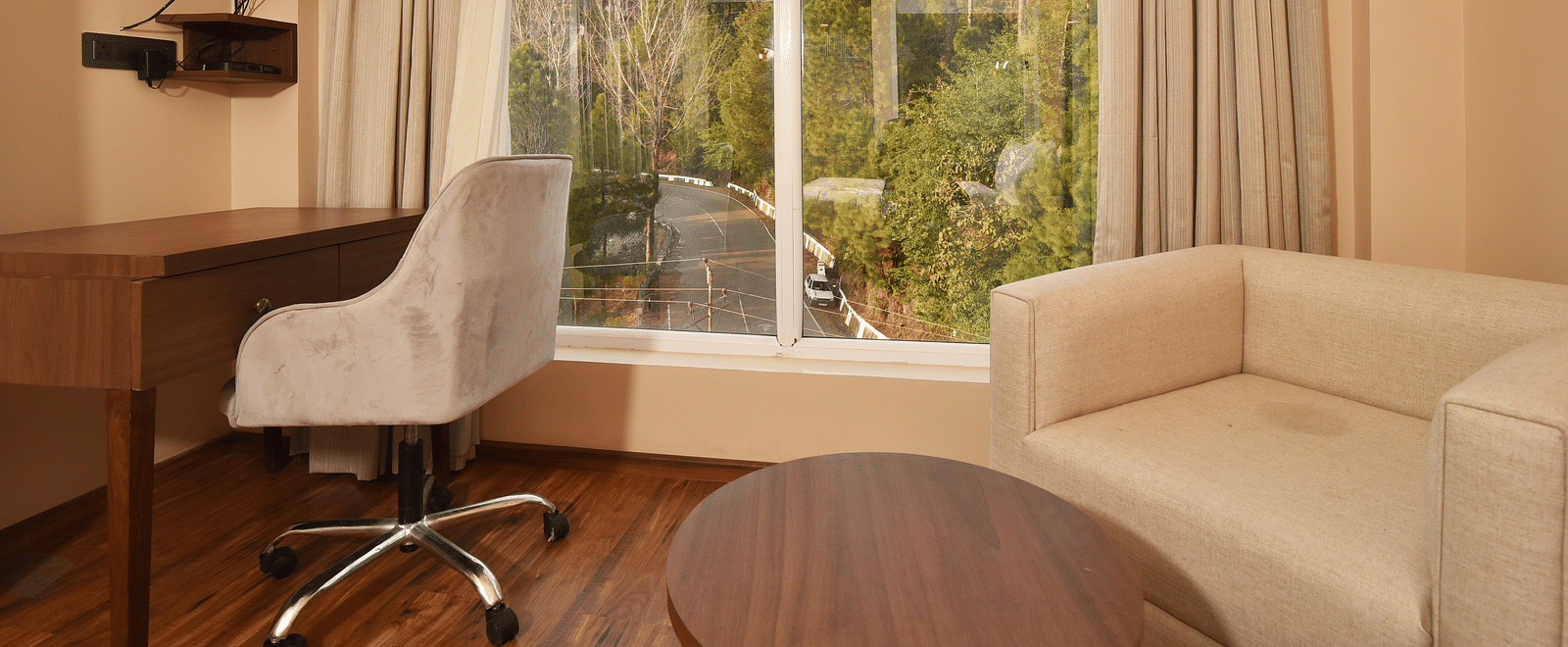 A modern seating area with a comfortable sofa, a work desk, and large windows providing a clear view of the surrounding landscape and mountains.