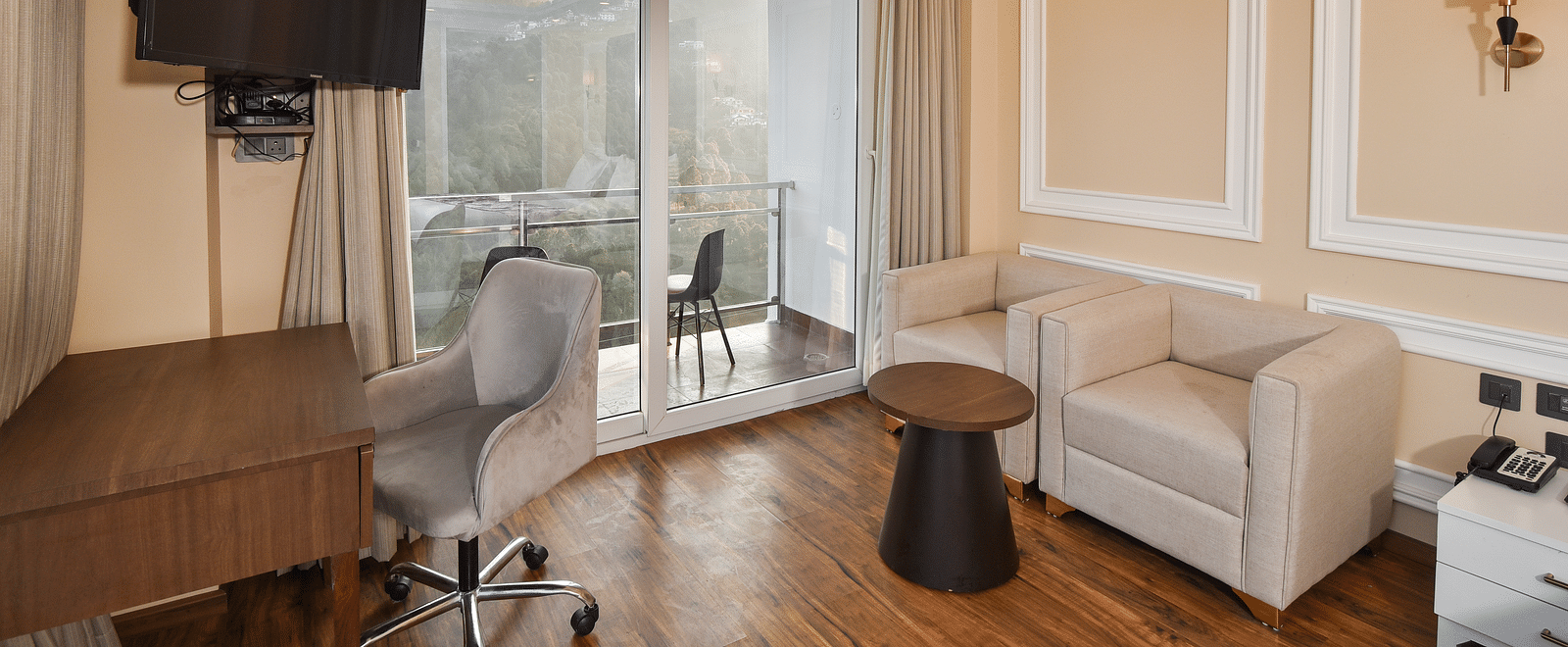 A modern bedroom with a king-sized bed, a seating area by the window, and large glass windows providing expansive views of the mountains.