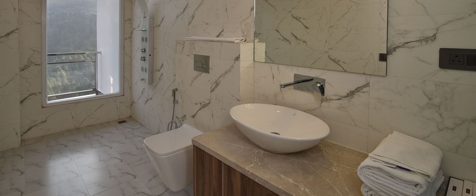 A sleek and modern bathroom with a marble countertop, a round sink, and contemporary fixtures. Large windows allow natural light to illuminate the space.