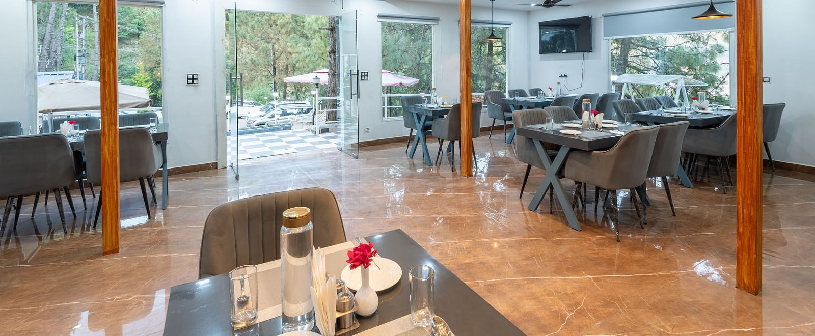 Bright and modern restaurant dining area with neatly arranged tables, grey chairs, large windows, and an open mezzanine level - DLS Nature Trinket Resort, Dalhousie.