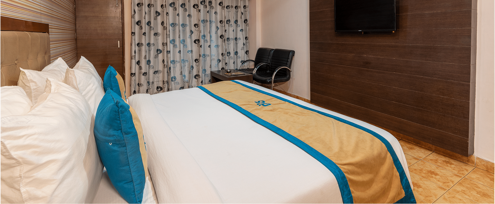 Side view of a Deluxe Non view room at DLS Spring Valley resort  Dharamshala featuring a  king bed, table, chairs and a TV