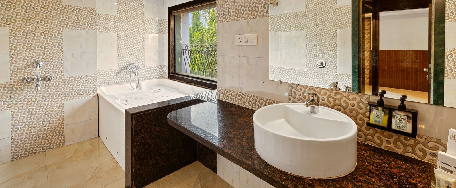 Contemporary bathroom with a wide mirror, wash basin, a large bathtub, and beige tiled walls at Mayur Retreat.