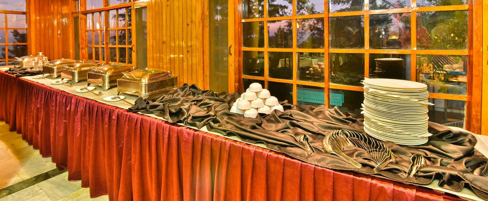 Close up view of buffet area with plates, bowls, and cutlery at DLS Hillcrest Resort, Shimla.