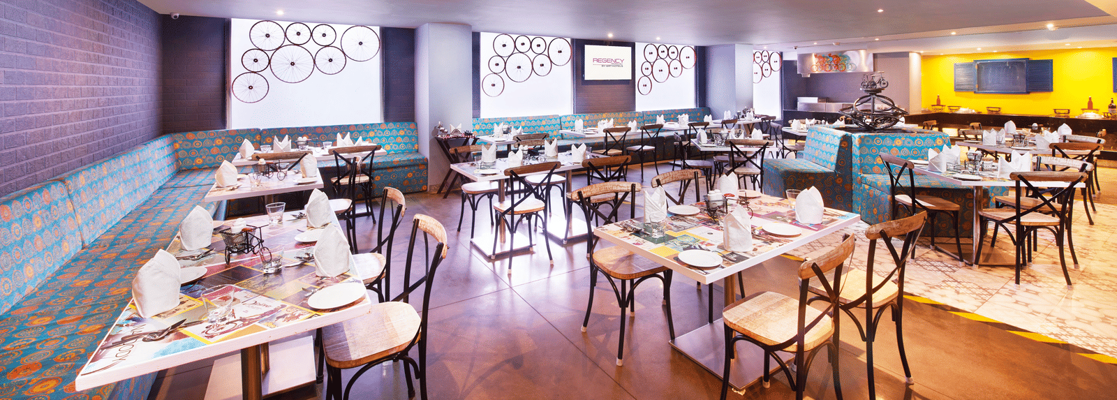 A brightly lit restaurant with chairs, a long bar counter, and a colourful wall mural | Regency Hotel near Tirunelveli Railway Station by GRT