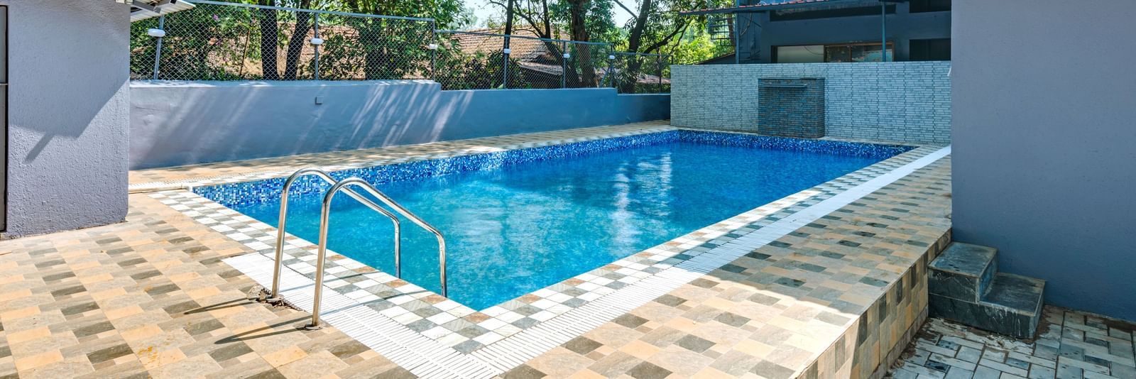 Outdoor swimming pool surrounded by trees and tiled flooring at Emerald Retreat, Tungarli.