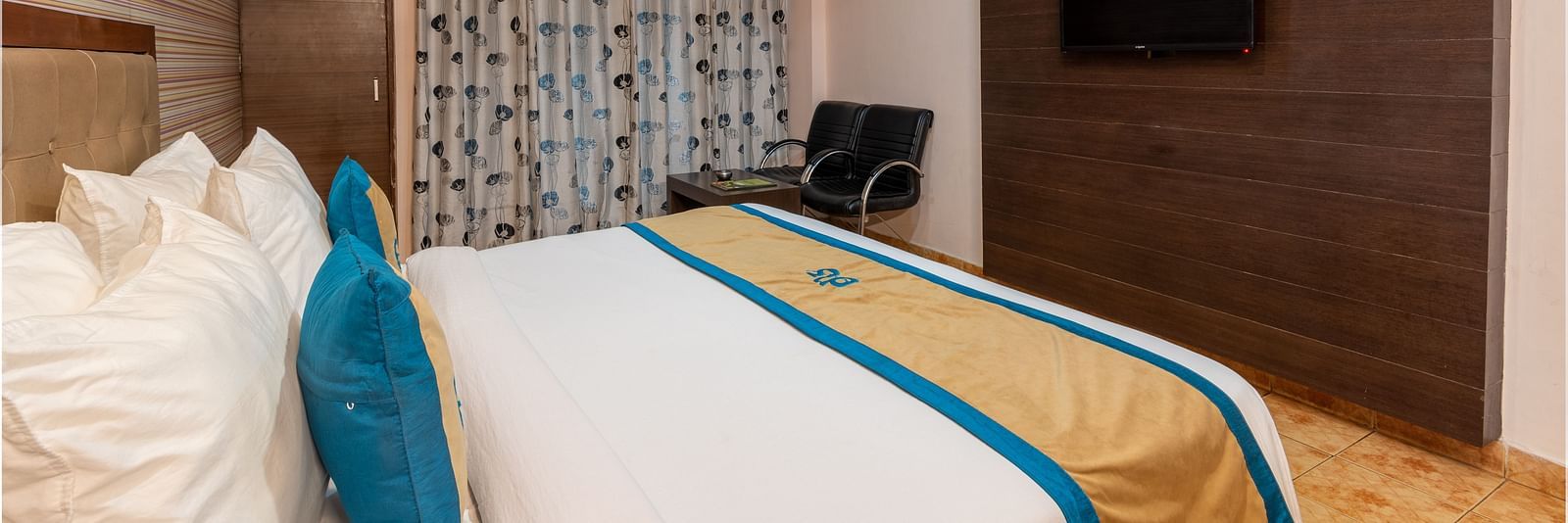 Side view of a Deluxe Non view room at DLS Spring Valley resort  Dharamshala featuring a  king bed, table, chairs and a TV