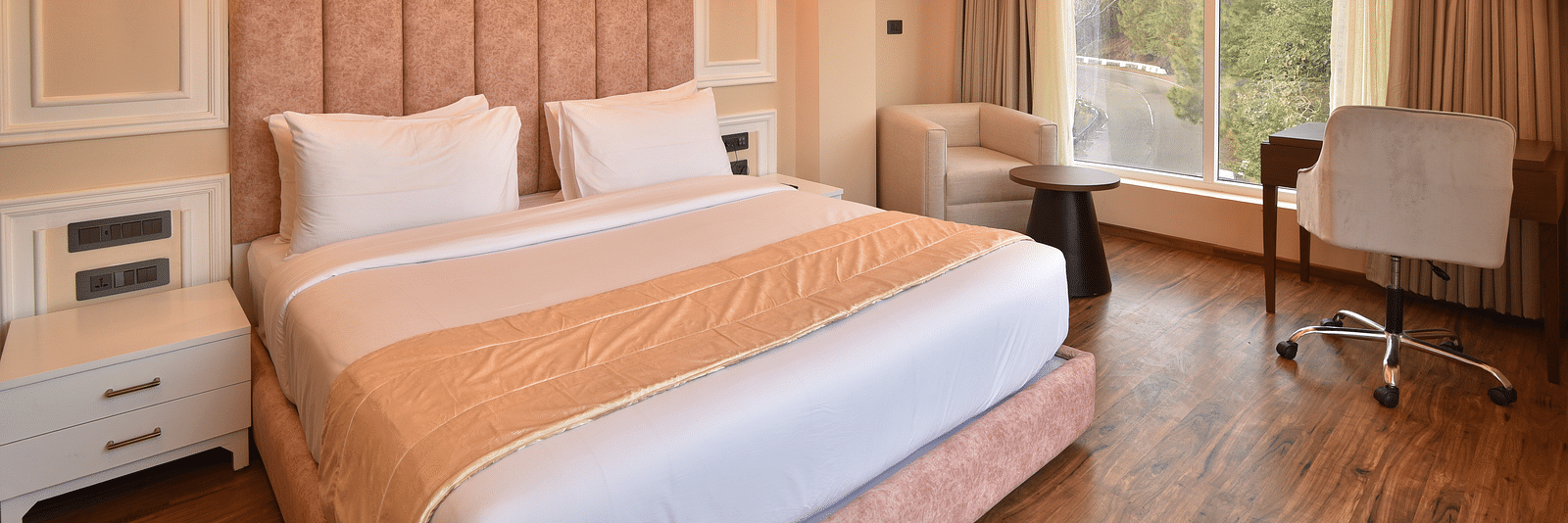 A modern hotel room with a king-sized bed, featuring soft lighting and large windows that offer stunning views of the surrounding hills and landscape.