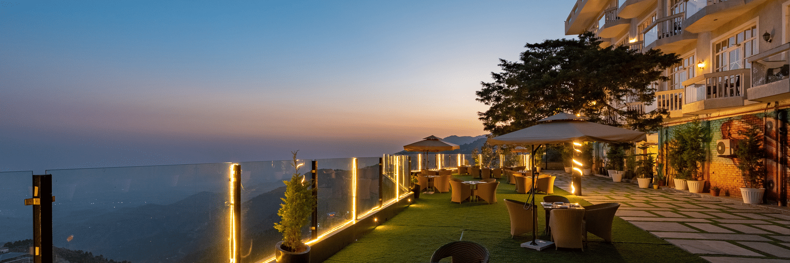 Facade view of DLS Highland Resort and Spa, Mussoorie with comfortable chairs in the lawn at dusk.