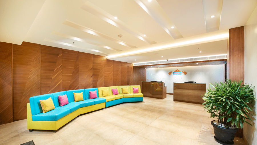The reception area has a large sofa, a wooden front desk, and decorative plants - Zibe Luxe Hyderabad by GRT Hotels