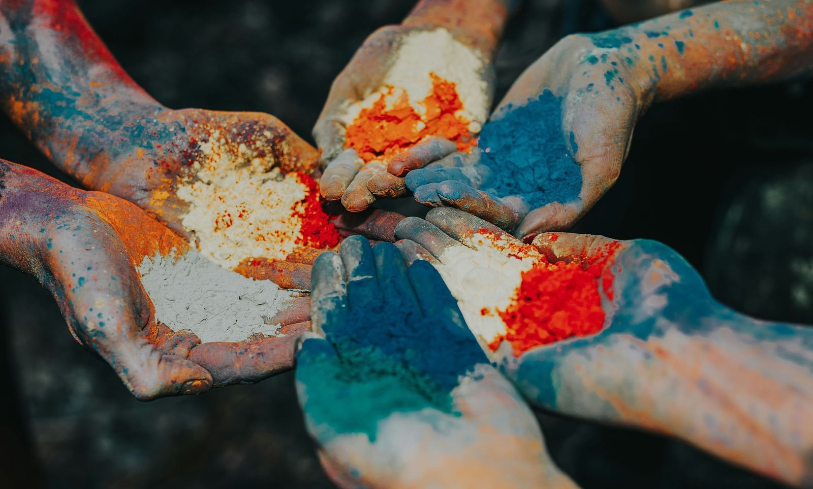Five hands holding Holi colours