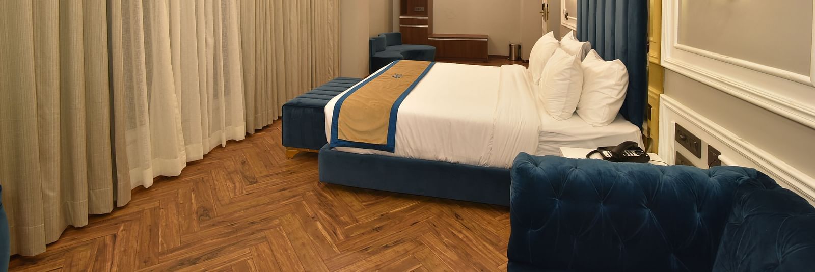 A stylish bedroom with a large bed and a seating area. The room features soft lighting, with large windows showcasing panoramic views of the surrounding hills.