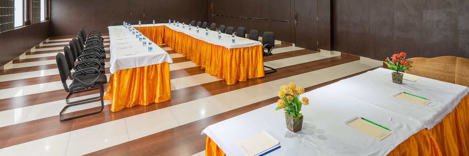 A conference room with a long table, chairs, and decorative flowers on the table. The room features wooden paneling and a checkered floor - DLS Meghavan Resort, Dharamshala
