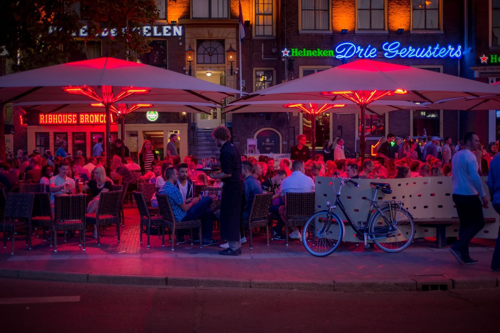 Many people sitting in an outdoor restaurant with neon lights above them.