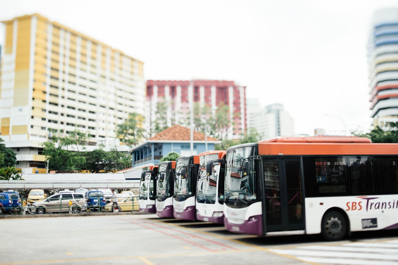 Busses parked in the bus depot with building in the background.