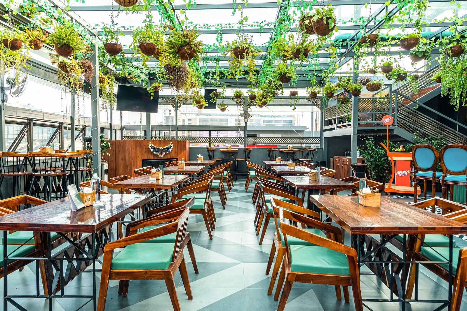 With plants hanging from the roof and wooden chairs with green cushions at Kyba restaurant at Visthara - Urban Boutique Hotel 10