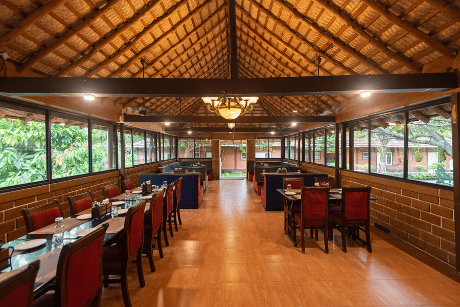 Chairs and tables on either side and a chandelier hanging from the bricked roof in the centre in the Aqua Restaurant at Ibex River Resort, Pollachi.