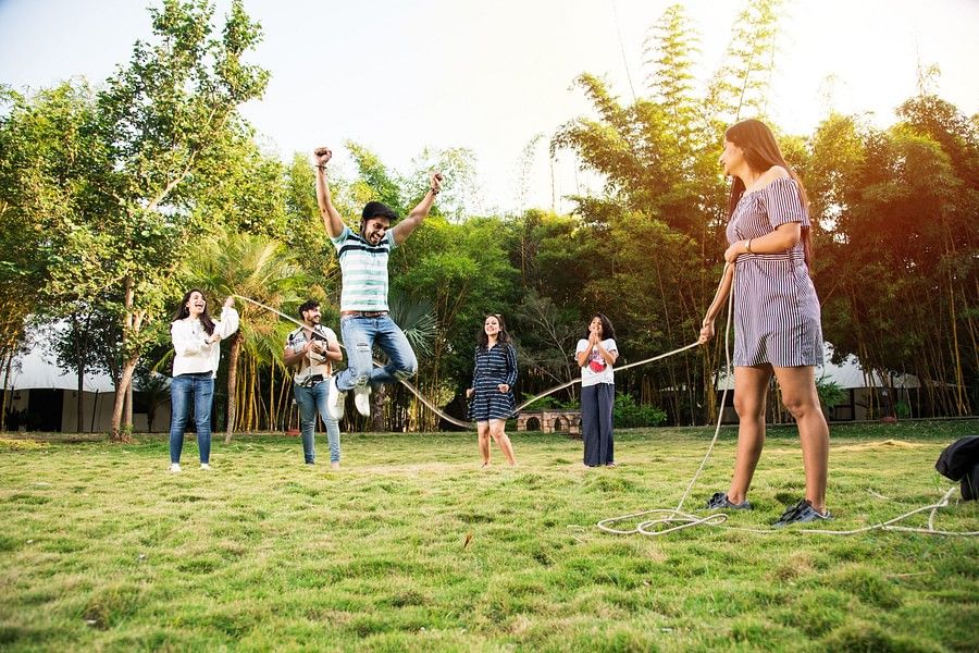 A group of adults and children playing tug of war in a grassy outdoor area, displaying joy and family bonding during a playful and competitive moment.