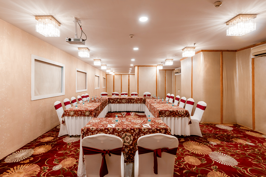 Conference room with a long hall setup featuring rows of covered chairs and tables for a large gathering at Mango Grove Hotel.