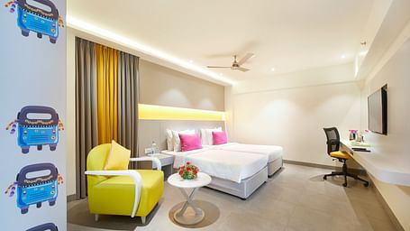 The spacious room features a large bed, a single loveseat near the bedside table, and a wall-mounted television across from it