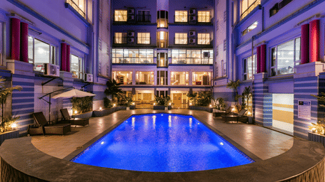 Long view of a swimming pool at Mayur Retreat and Spa surrounded by hotel building.