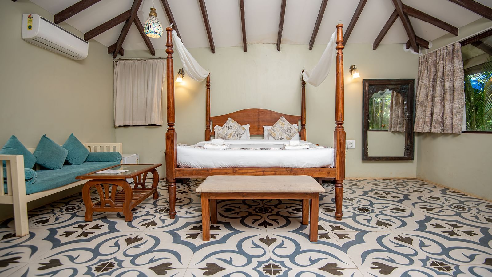 Spacious guest room with two sofas and a canopy bed under a sloped wooden roof at De Soul Santé, Morjim.