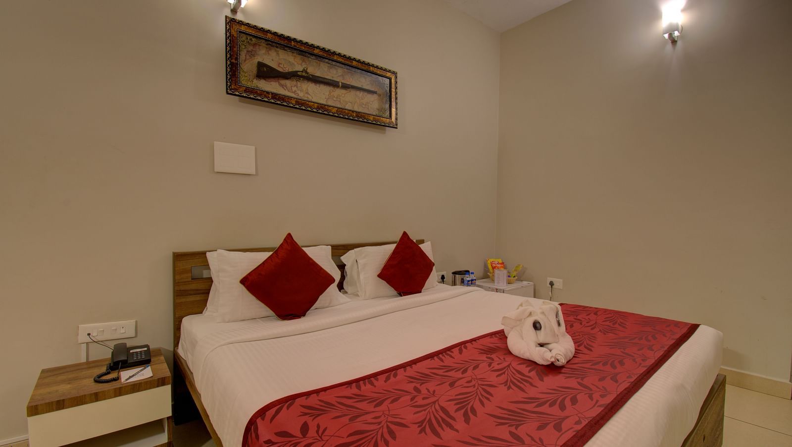 Bedroom with a huge bed, bedside table, and a decorative piece of a gun on the wall | Superior Room | Woodstock Resorts, Coorg
