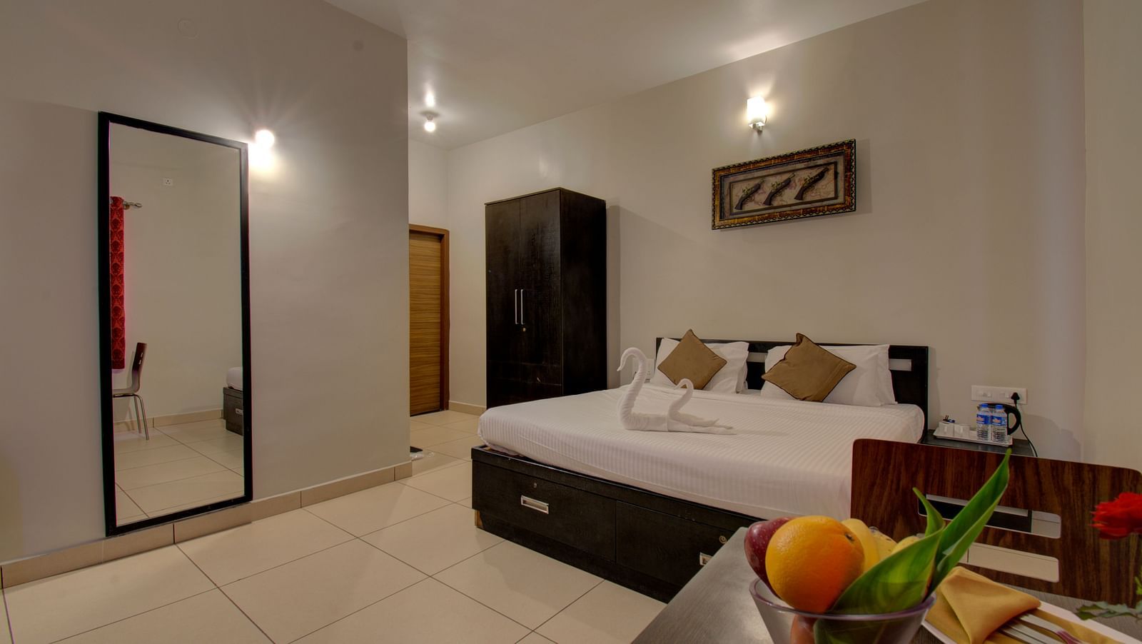 A bedroom with a huge bed, a mirror, Cupboard, a table with fruits on it | Superior Room | Woodstock Resorts, coorg