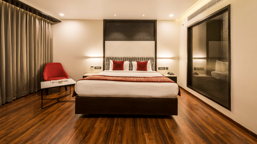 Club Room at The Citrine, Bangalore, with a king bed, grey upholstered headboard, red throw, red accent chair, and a dark wood floor.