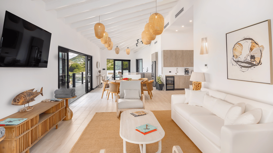 A living room at Tamarind Hills Resort and Villas, Antigua, with a sofa, wooden table, orange pendant lights, large windows, and a mounted television.
