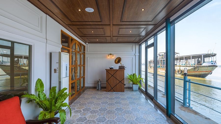 A bright reception area with wooden finishes and a vintage globe on a cabinet, plants in the corner, and a view of a boat through large windows.