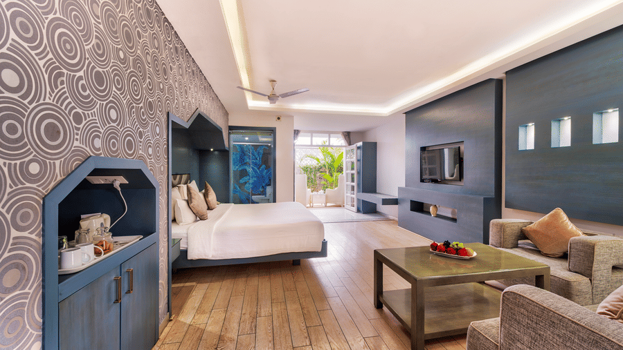 A spacious hotel suite featuring a bedroom area with a large bed and a separate living area with a sofa and coffee table - Grande Bay Resort & Spa, Mamallapuram
