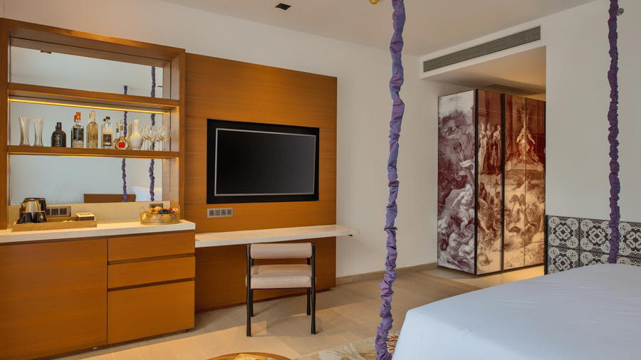 Deluxe Patio King Room featuring a plush bed facing the TV mounted on the wall and a work desk next to it with a minibar