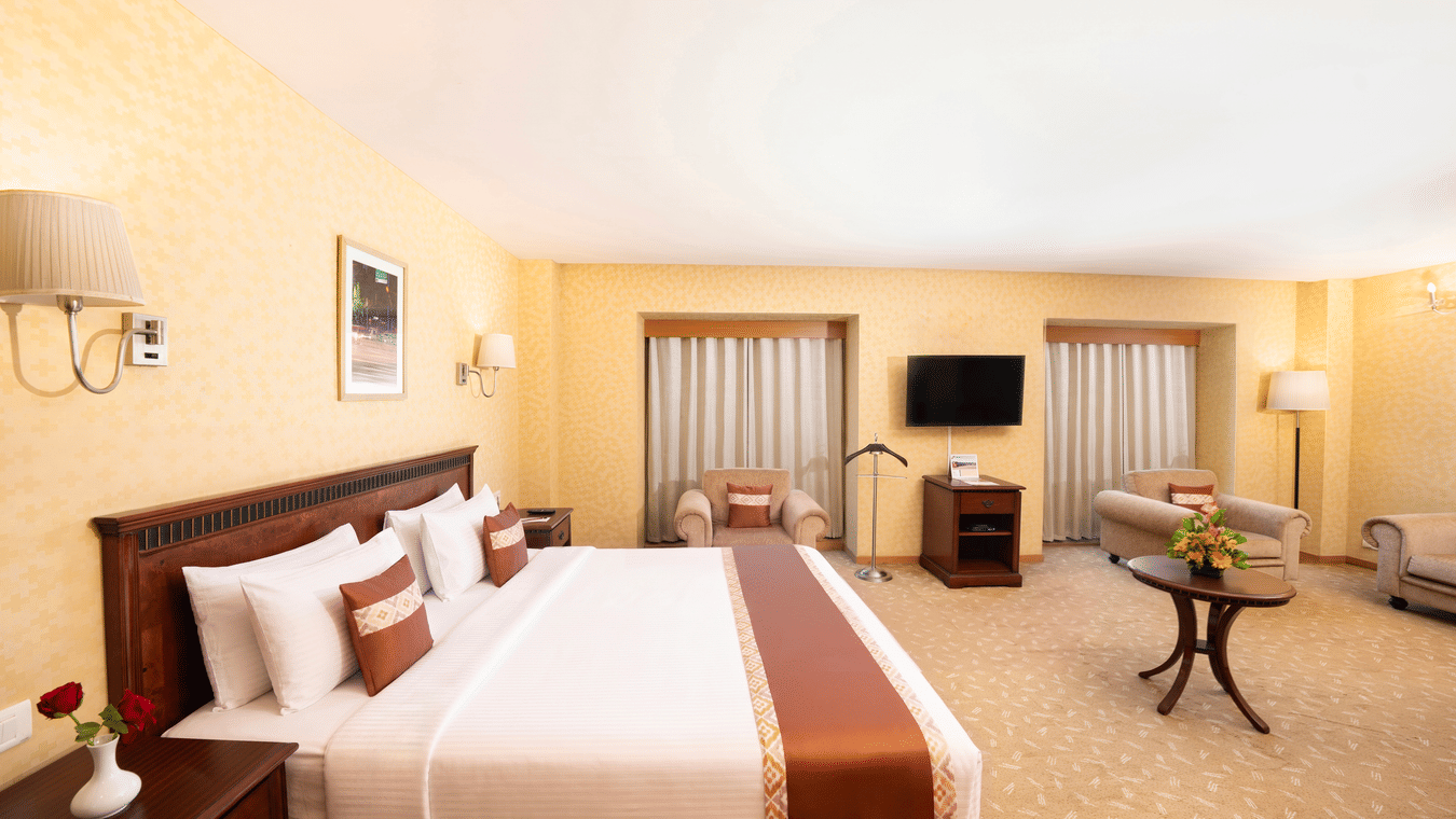 A room with a large bed, spreads, pillows, a table, a window, and a table. | MGM Mark Whitefield