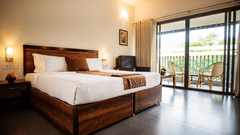 Bright bedroom at Abad Green Forest, one of the finest cottages in Thekkady, featuring wooden furnishings, crisp white bedding, and a balcony overlooking lush greenery.