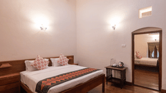 The warmly lit Mayfair Suite at Ibex Resorts, Coonoor (Leewood), with a large bed, bespreads, pillows, and a mirror..