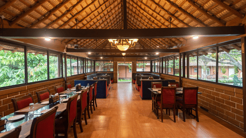 Chairs and tables on either side and a chandelier hanging from the bricked roof in the centre in the Aqua Restaurant at Ibex River Resort, Pollachi.