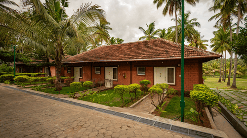 Facade view of the suite at Ibex River Resort, Pollachi, with small manicured gardens and coconut trees in front of it.
