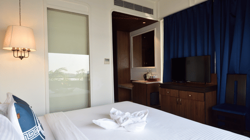 a well made bed with blue pillows with a tv opposite it - polo floatel kolkata