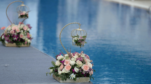 Flower arrangements with pink and white roses sit on the edge of a swimming pool.