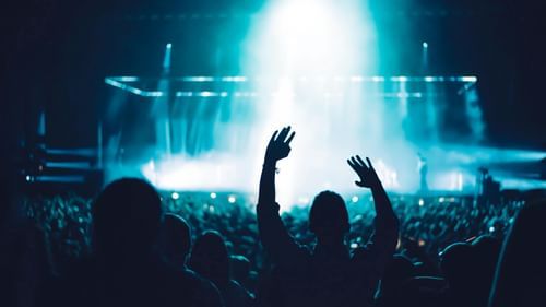 Audience raising hands towards a brightly lit stage during a live performance.