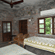 The Bird's Eye View Eco Cottage bedroom with rustic stone walls, wooden windows, and a double bed at Wild Brook Retreat, Rajaji National Park.