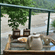 A teapot, 2 cups and snacks on a balcony table overlooking a wide river and green hills.