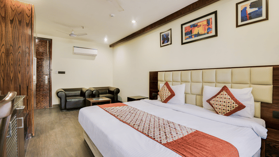 A spacious room with a large, well-made double bed, a cupboard and a seating area beside the door - Hotel Bluestone Prime (Nehru Place), New Delhi