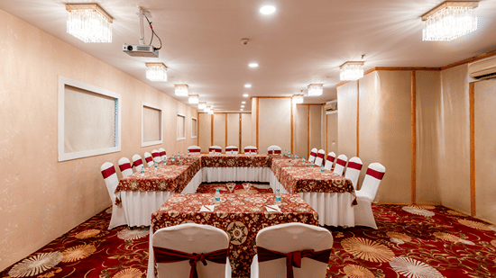 Conference room with a long hall setup featuring rows of covered chairs and tables for a large gathering at Mango Grove Hotel.